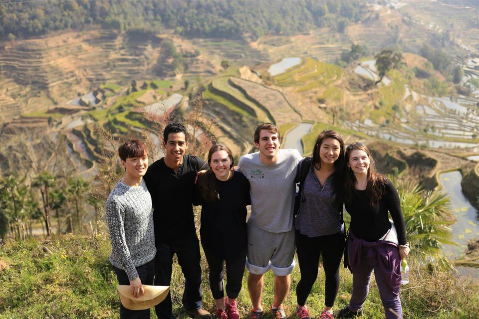 Students stand on a hillside overlooking a valley with terraced fields.