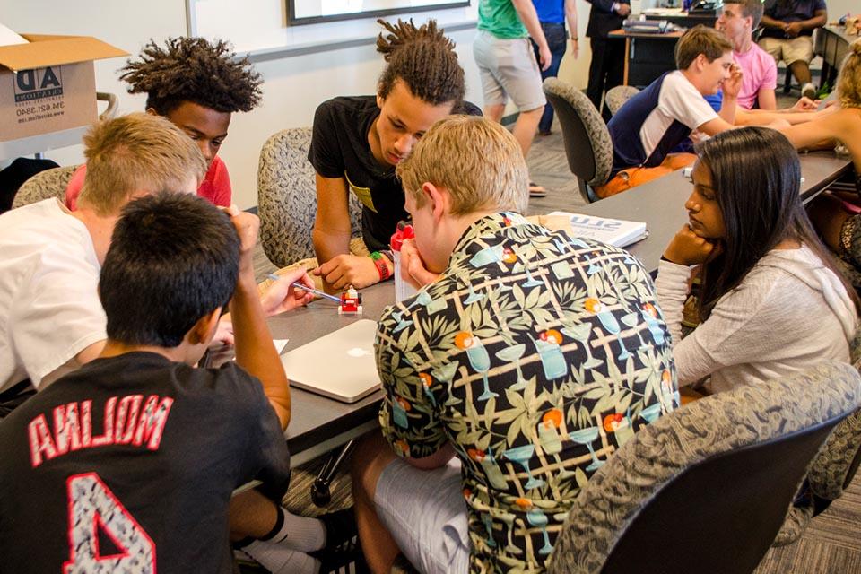 Student particpating in the Allsup Entrepreneurship Academy huddle around a table while they work together to solve an innovation challenge.