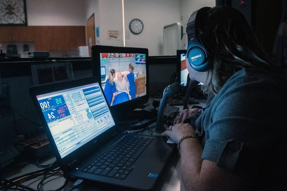博彩网址大全护理系学生戴着耳机在模拟护理程序监视器上复习视频