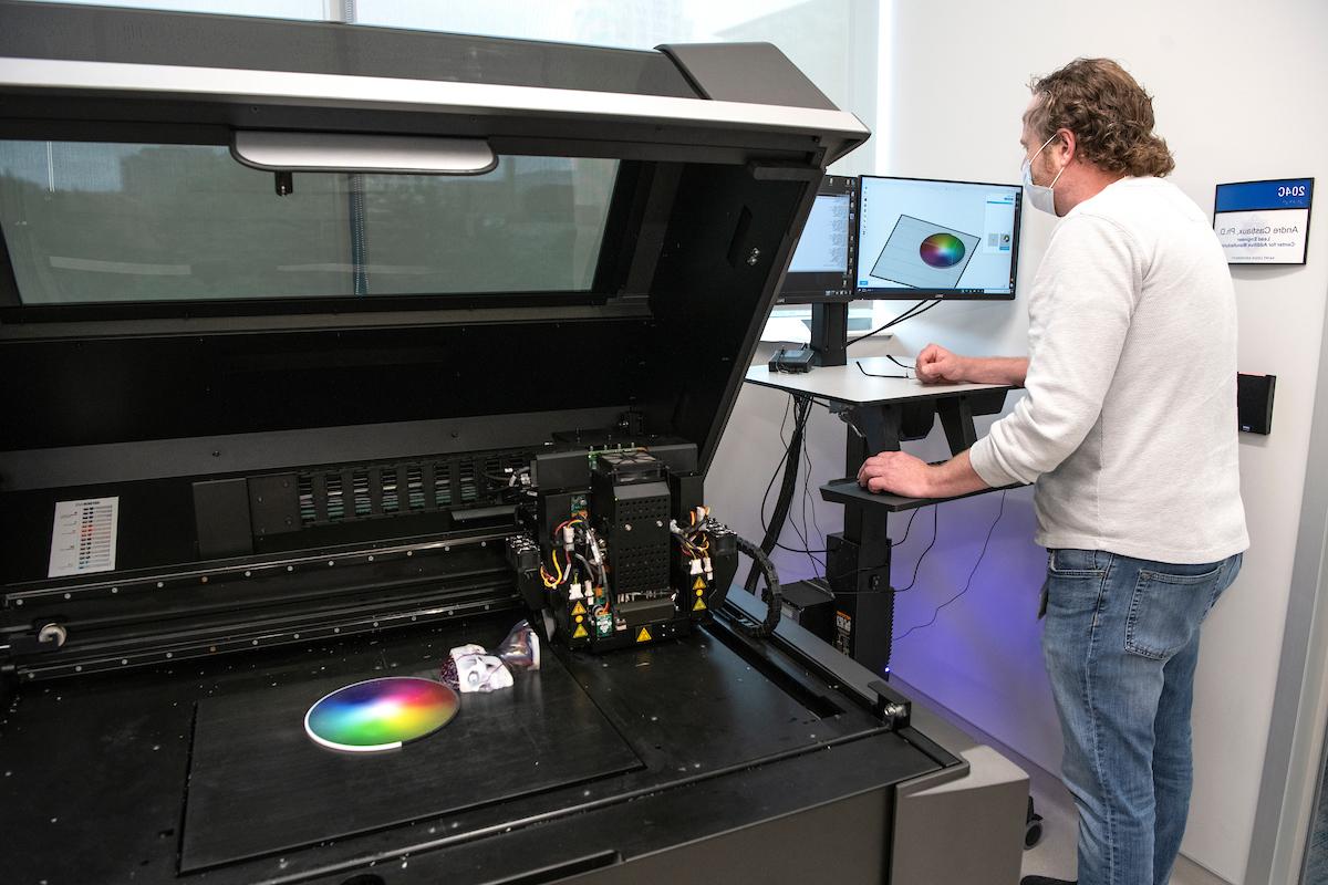 个人站在3D打印机旁边的电脑前