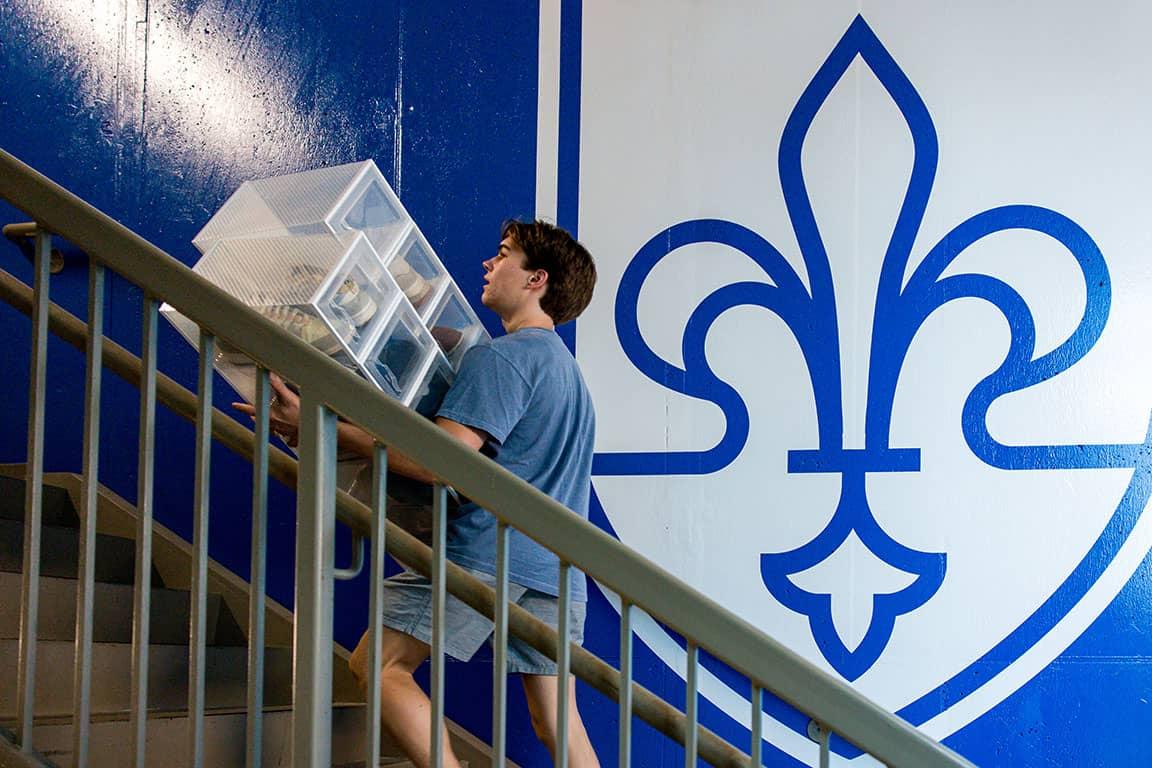 一名学生在博彩网址大全盾牌的壁画前拿着他们的物品上楼
